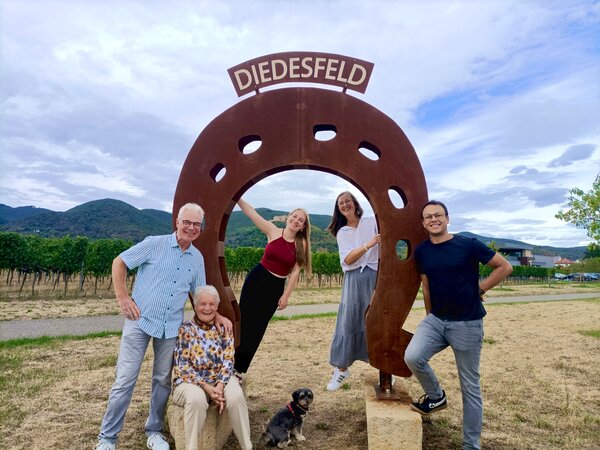 Gastgeberfamilie Ehmer und Hoefer vom Gästehaus an der Weinstraßenmitte Matthias, Marianne und Nicole Ehmer mit Theresa und Daniel Hoefer und Hund Dori vor dem Hufeisen-Denkmal „Diedesfeld“ in den Weinbergen