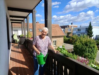 Blumenbalkon am Gästehaus an der Weinstraßenmitte Marianne Ehmer gießt mit einer grünen Gießkanne die Blumen auf dem langen Holzbalkon des Gästehauses